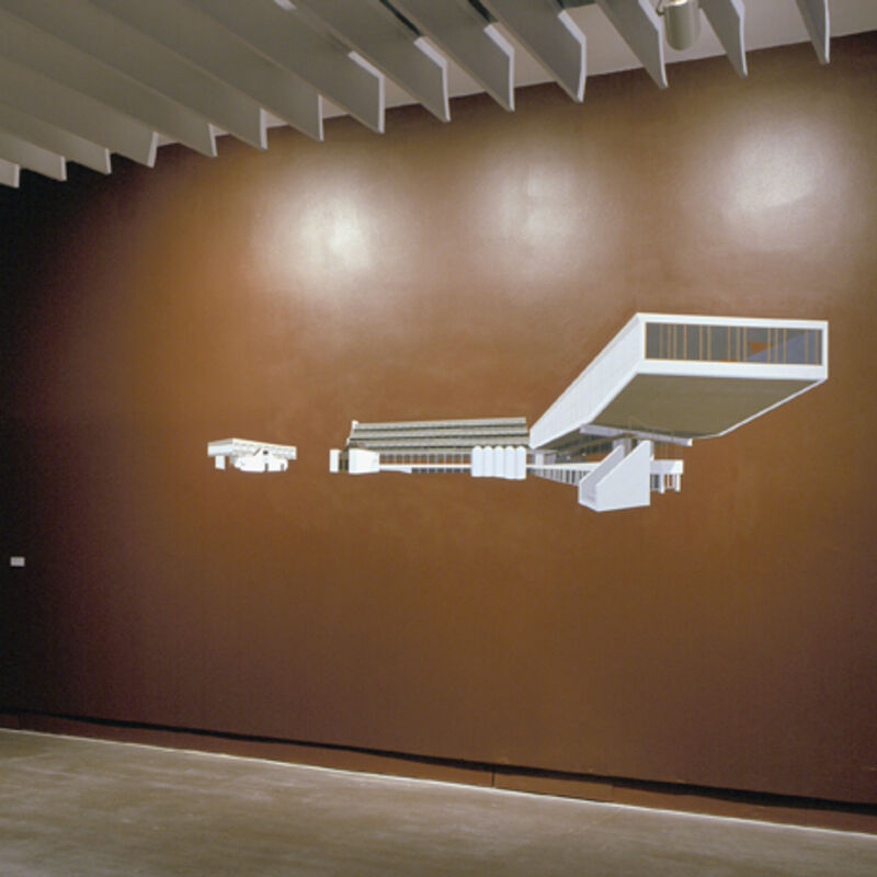 From Beyond / Photographs, the gallery wall is brown. There is a white painting of a futuristic building on the walls.