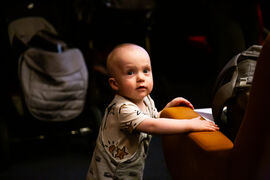 A cute baby standing up, holding on to an orange cinema seat for support.