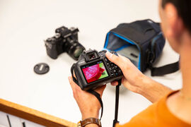Person holding a digital camera and looking at the screen on the back of it which shows an image of a flower