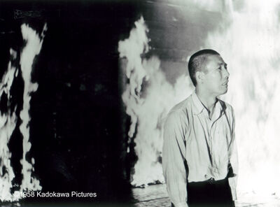 A black and white photograph shows a distressed man standing next to a burning building