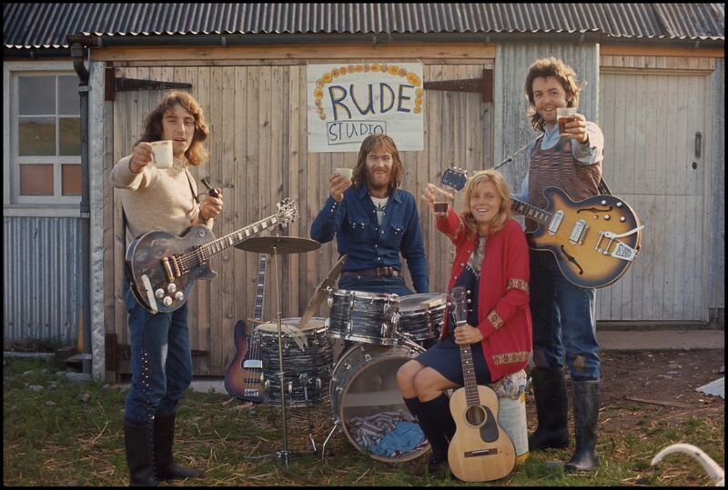 Paul McCartney and his other band members cheers cups while sitting outside with their musical instruments