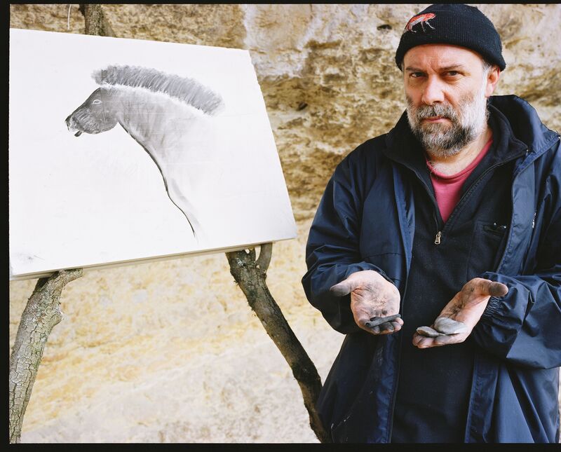 A man with dirt on his hands stands next to a pencild rawing of a horse