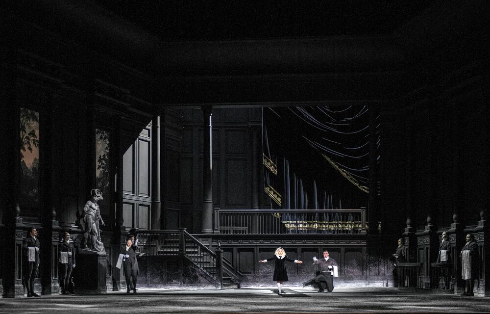 A girl with blonde hair and a black dress on a dramatic black stage set