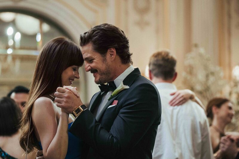 A man in a suit and a woman in a blue dress smile and dance together closely