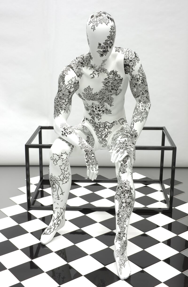 A mannequin who is decorated with intricate black patterns sits on a table in Johanna Basford's exhibition.