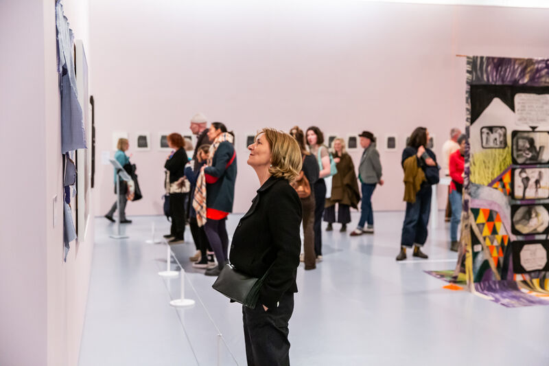A busy gallery space with people looking at the works on the wall