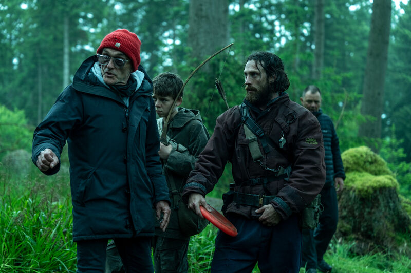 A group of people wearing survivalist clothes talk to each other in a green forest.