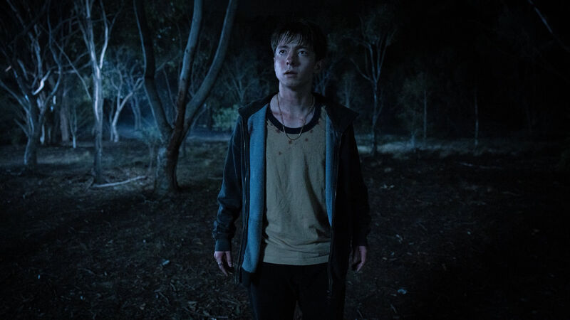 A teenage boy stands alone in dark woods