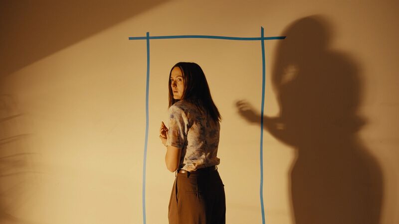 A woman with dark hair stands by a door outline drawn on a blank wall.