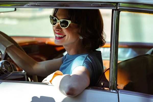 A woman in sunglasses drives a car with the window down.