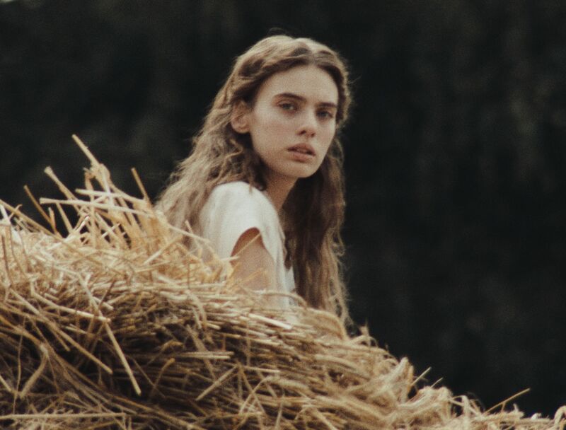 A young woman sits on some hay and looks into the camera