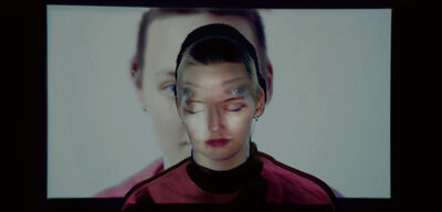 A young woman stands in front of projected image of herself