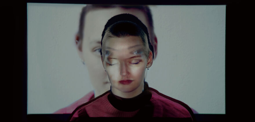 A young woman stands in front of projected image of herself