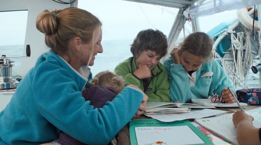 Two children doing school work with their mother on a boat