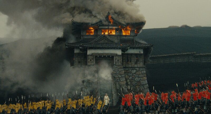 The gates to a Japanese city burn while groups of soldiers converge.