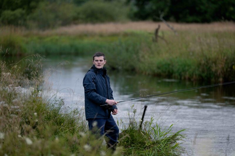 A man stands by a riverside fishing