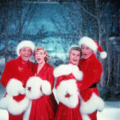 Two men and two women in festive red costumes, singing in a snowy scene
