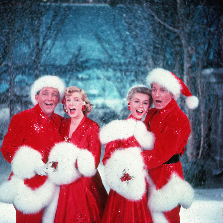 Two men and two women in festive red costumes, singing in a snowy scene