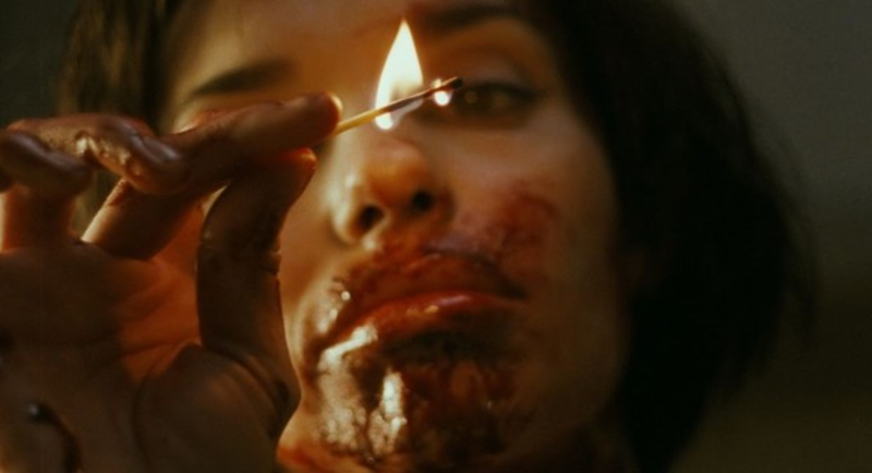 @omen holding a lit match in front of her bloody face