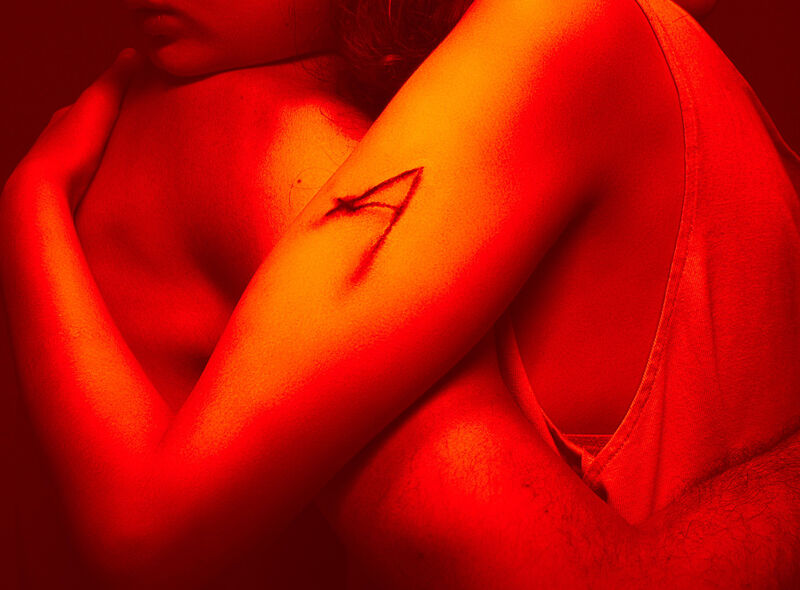 Two arms embrace, one with an 'A' carved into the skin. The image is filtered heavily in red.