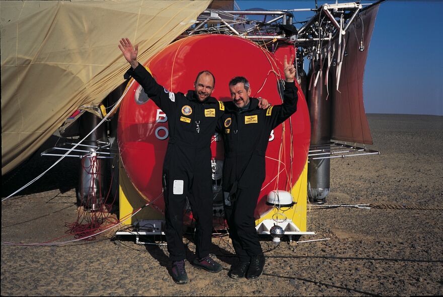 Two men wave in front of their hot air balloon