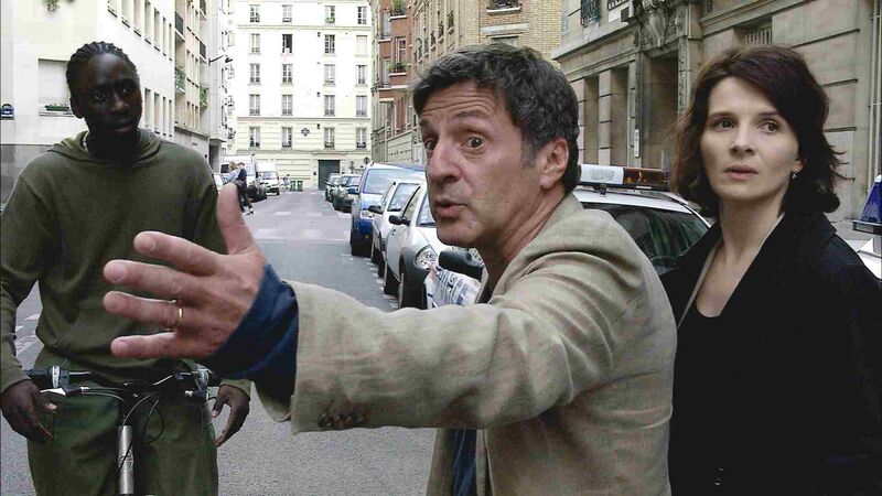 A man stands in the street, looking angry and gesturing with his arm. Two people stand next to each other.
