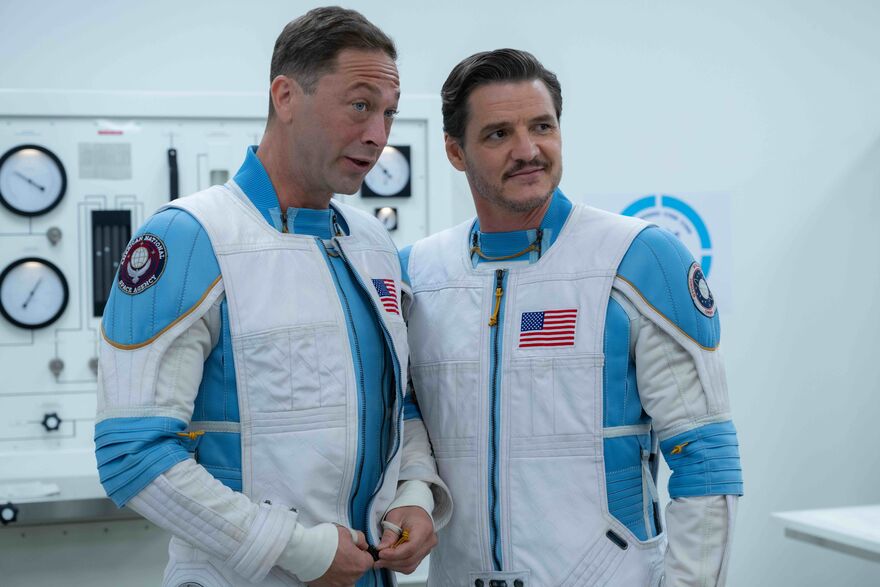 Two men wearing white and blue space suits stand next to each other smiling.