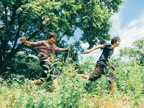 Two boys run through a forest.