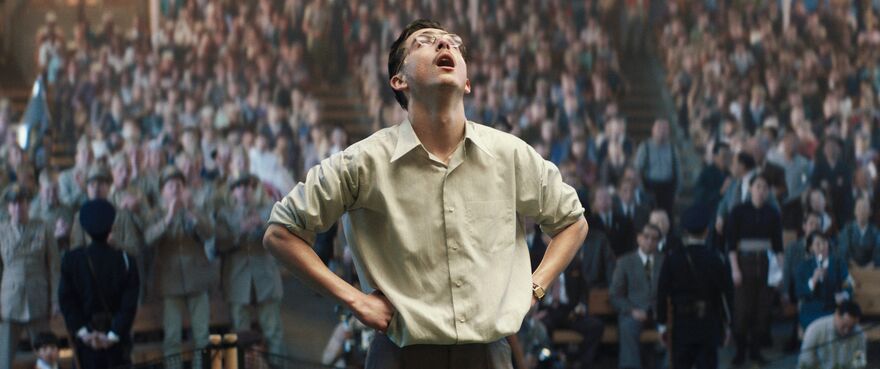 A man stands either his hands on his hips looking up at the sky while people applaud him