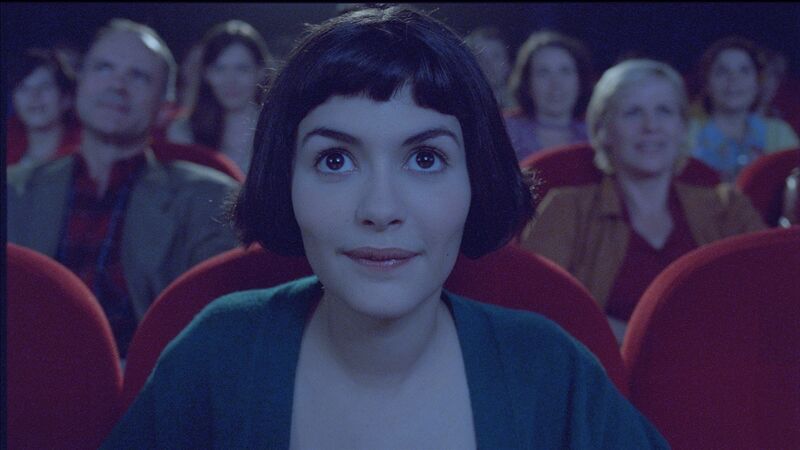 Amelie, with dark hair, sits in a cinema, smiling.