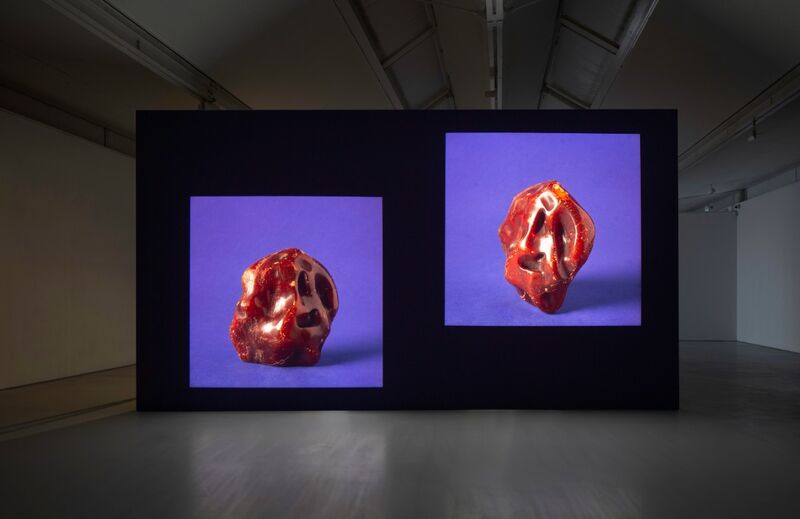 A still from Stuart Whipp's exhibition shows two images of unusual red stones against a blue backdrop.