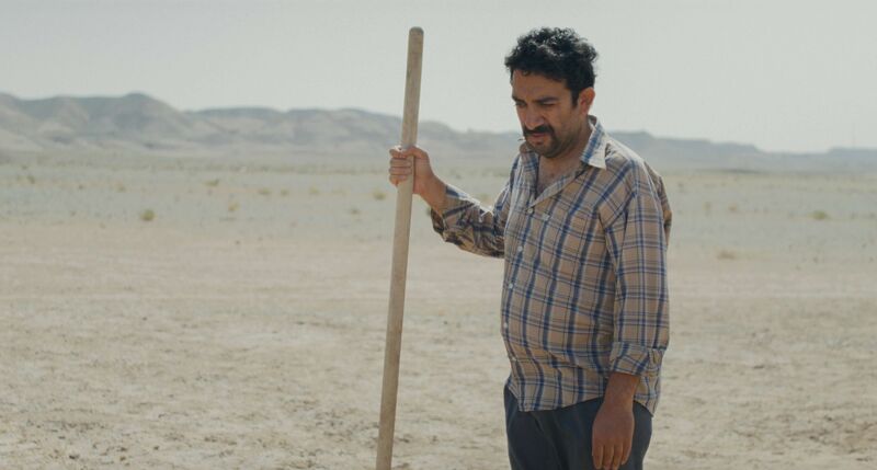 A man holds a shovel in the middle of the desert