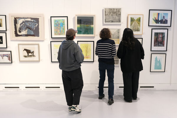 Three people looking at framed prints on the wall of DCA Centrespace