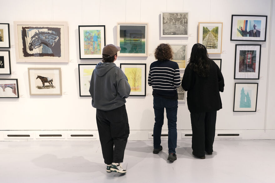Three people looking at framed prints on the wall of DCA Centrespace
