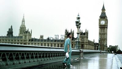 A man in hospital clothes walks across a bridge next to Big Ben, on an entirely deserted day.