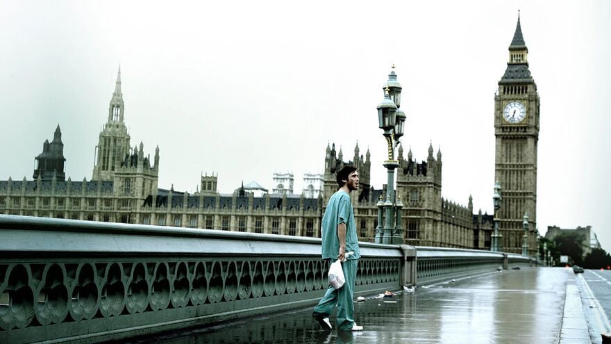 A man in hospital clothes walks across a bridge next to Big Ben, on an entirely deserted day.