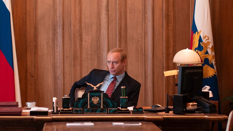 Jude Law as Vladimir Putin, sits at a desk.