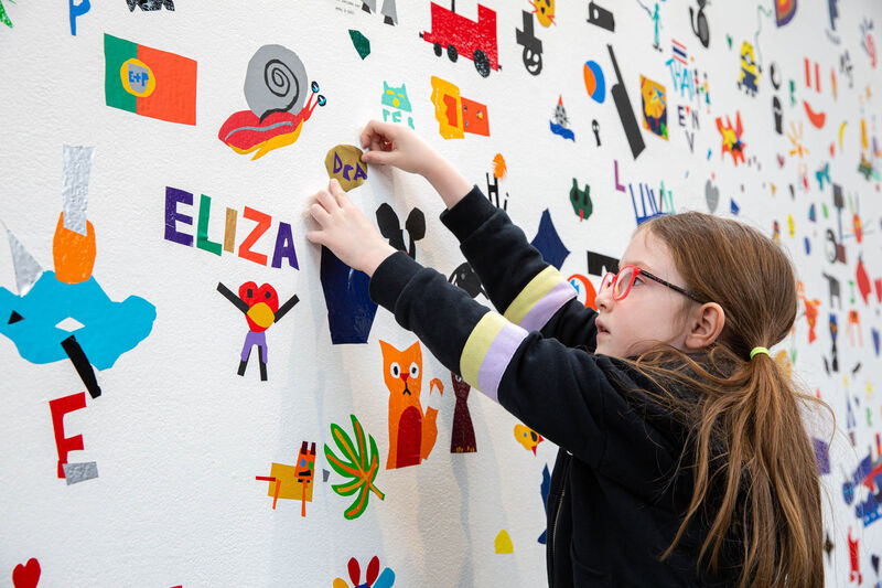 Child sticking vinyl to the wall outside of Gallery 1 to create a giant mural