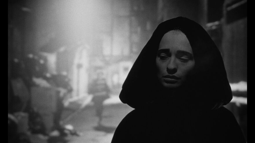 A woman in a cape walks towards the camera while a figure chases her in the distance