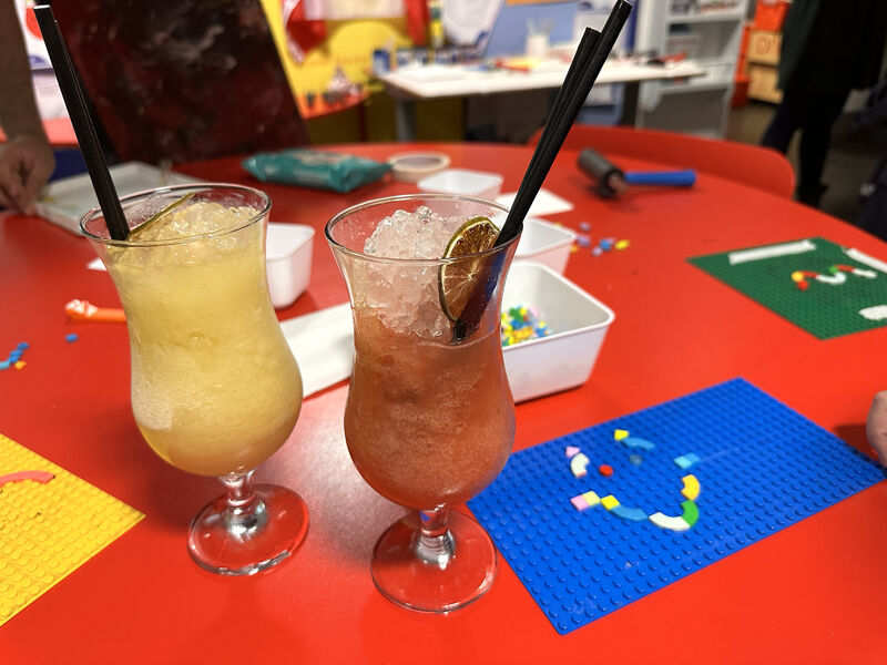 Two cocktils on a table surrounded by people making lego dot designs for printing