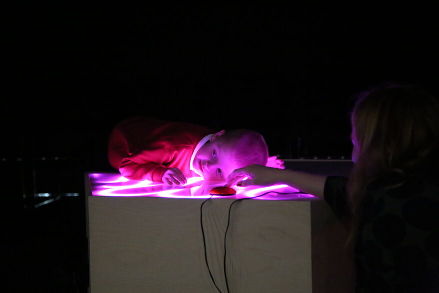 Child leaning their head on a Soundplay installation which is glowing pink