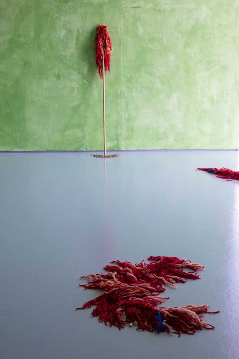 A gallery with green mottled walls. Various objects, made from red fabric, appear on the floor and walls. 