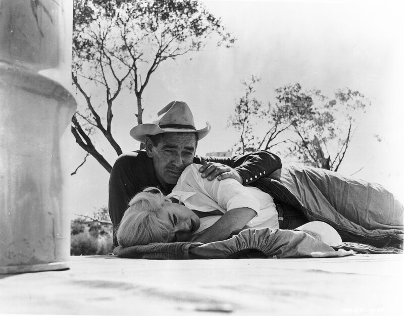 Marilyn Monroe lies on a ground, embraced by a cowboy