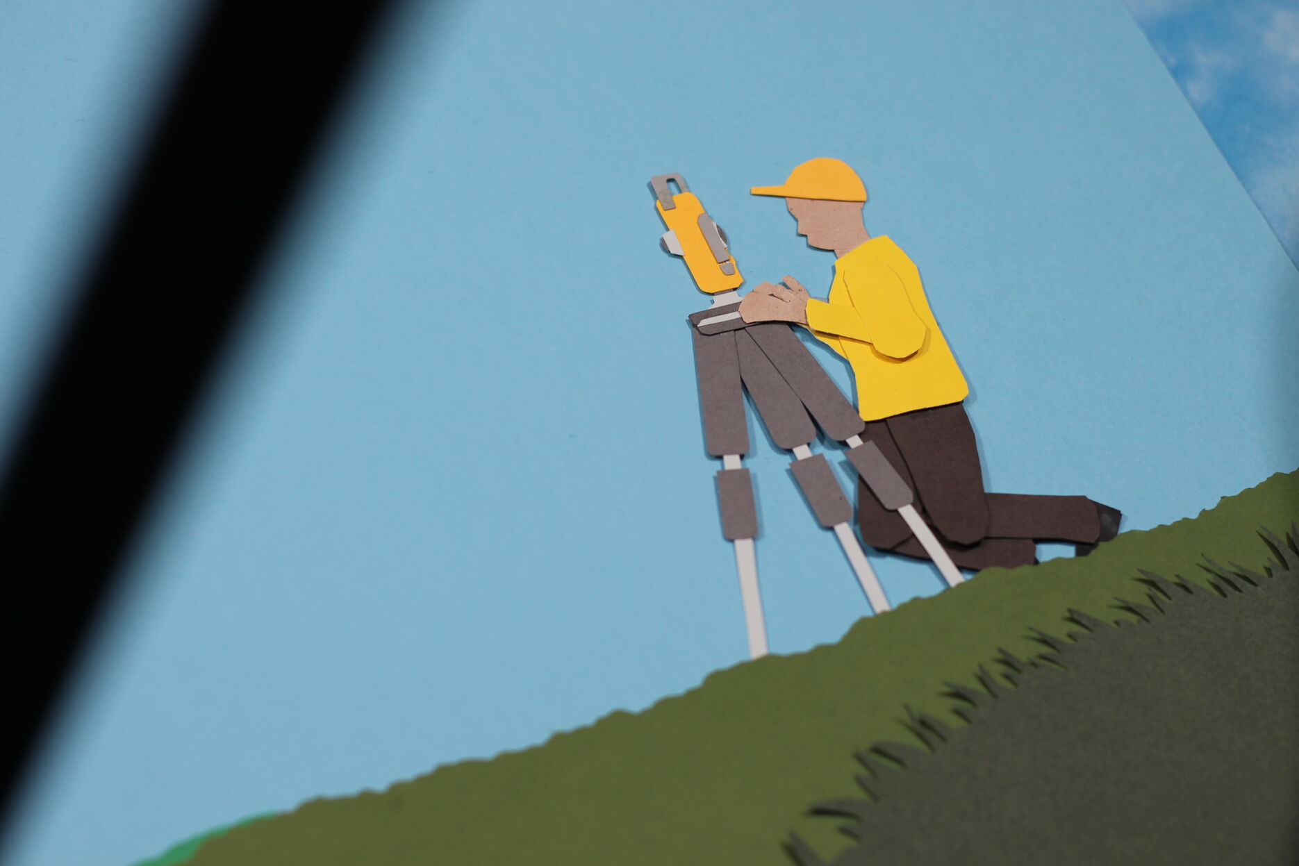 A still from an animation made out of cut paper. A man operates a film camera in the image.