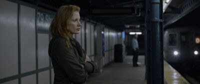 A woman with ginger hair stands with her arms crossed on a subway platform.