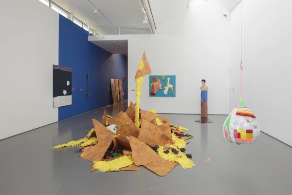 An image from 'Shonky: The Aesthetics of Awkwardness' shows a giant sculpture of cheesy nachos in the middle of the gallery floor. Next to it, a large colourful ball is suspended from the ceiling.