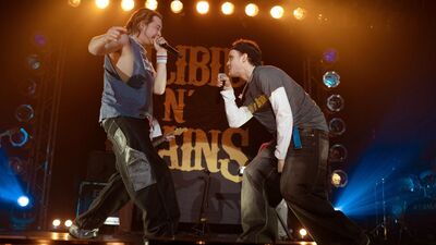 Two men wearing a hip hop-inspired clothing dance and sing on stage