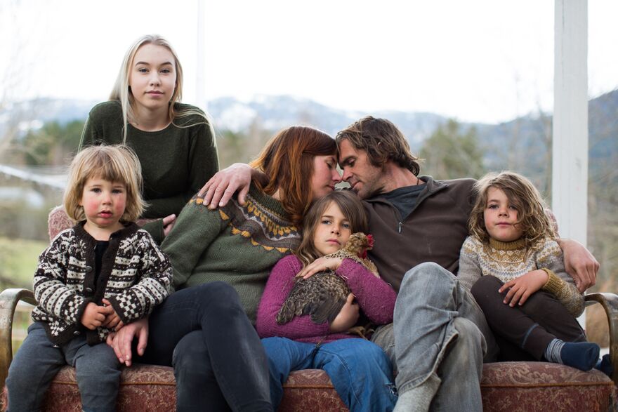 A family with three young children and a teenager sit outside on a couch. The couple have their foreheads together.