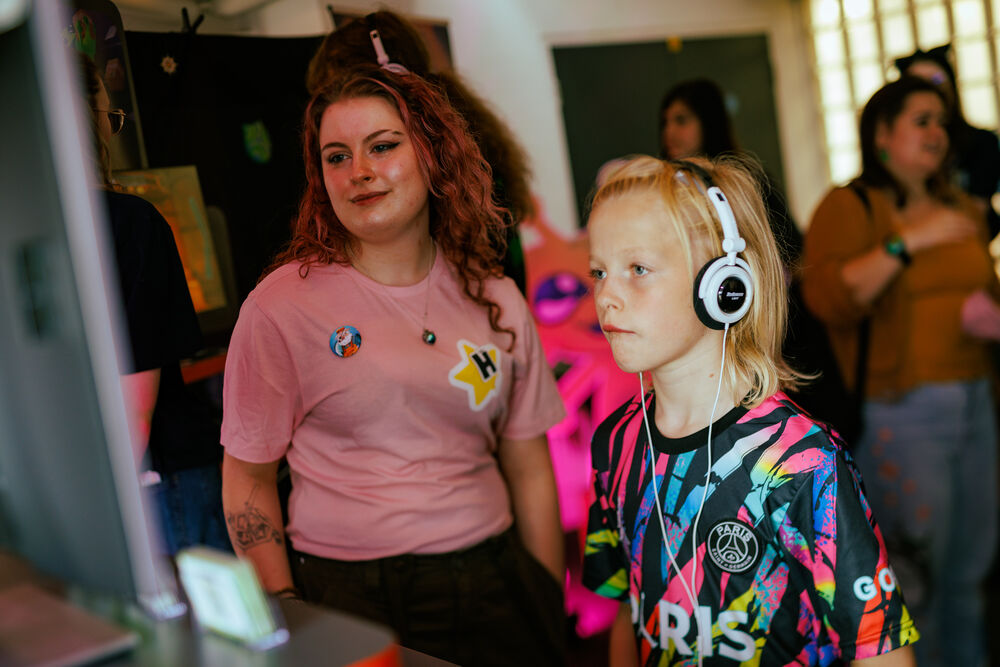 A child plays a video game at Drop in and Play while a game developer watches them and smiles.