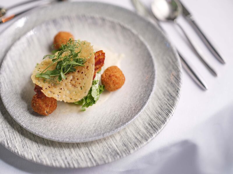 A fancy plate of food. The plate is grey and there is a knife and fork off to the righthand side